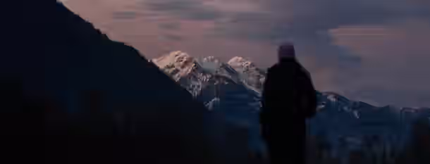 Ascending Heights: Path to Leadership Silhouette gazing at snow-capped mountains at dusk, symbolizing an emerging leader’s journey towards self-improvement and lofty aspirations.