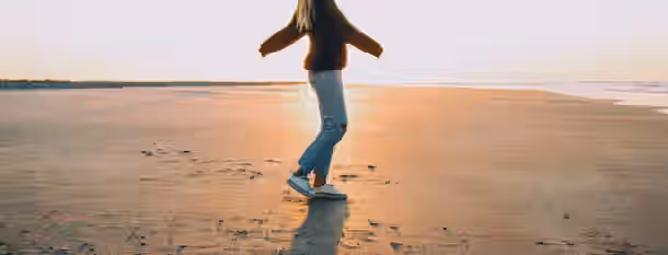 Path to a Brighter Horizon A woman dances barefoot on a serene beach at sunrise, symbolizing a leader embracing the journey to self-discovery and growth.