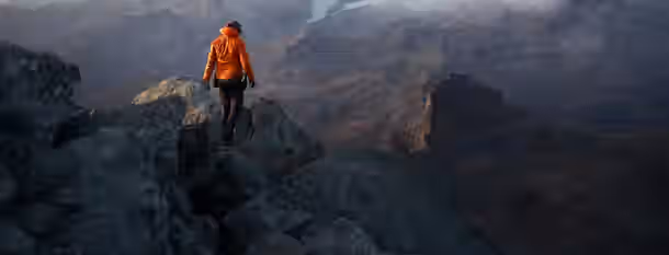 Ascending the Summit of Self-Discovery An individual in an orange jacket scales a rocky mountain, symbolizing the challenging yet rewarding journey to self-improvement and leadership.